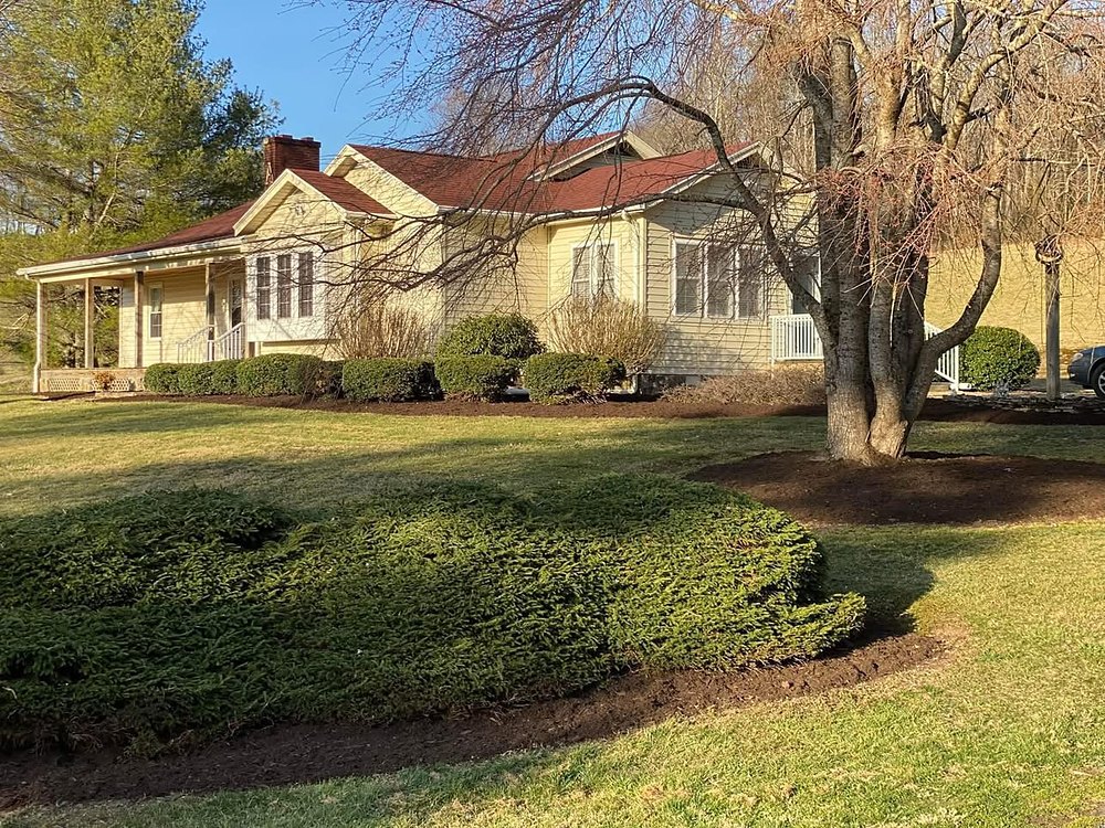 Manicured shrubs and fresh mulch beds framing a country ranch home, maintained by Cavalier Cleanup