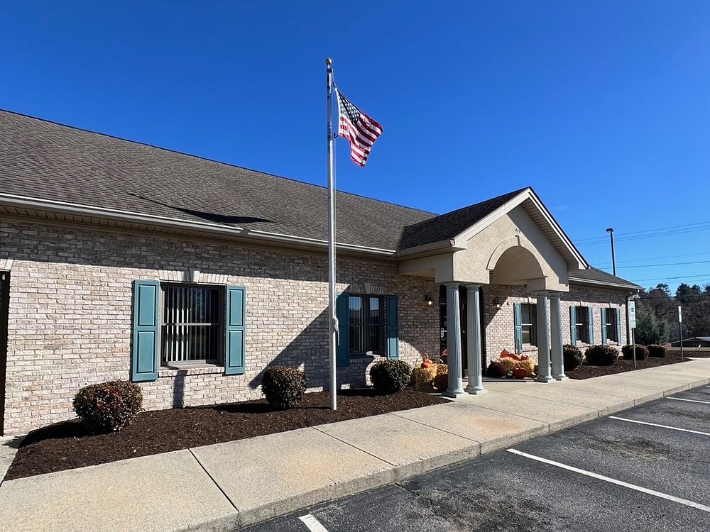 Fresh mulch beds and trimmed shrubs lining a brick office building with an American flag, maintained by Cavalier Cleanup