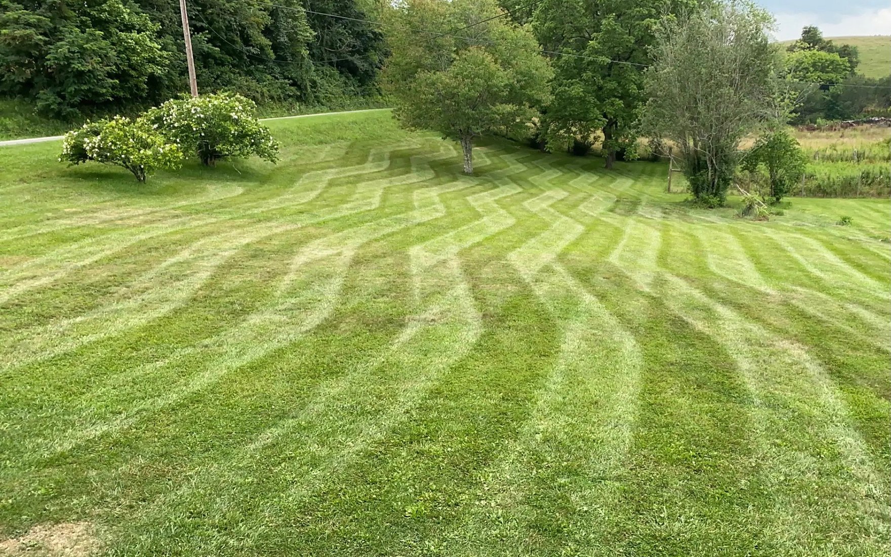 A wide hillside lawn in Hillsville, VA freshly mowed in clean stripes by Cavalier Cleanup, with treeline and mountains beyond