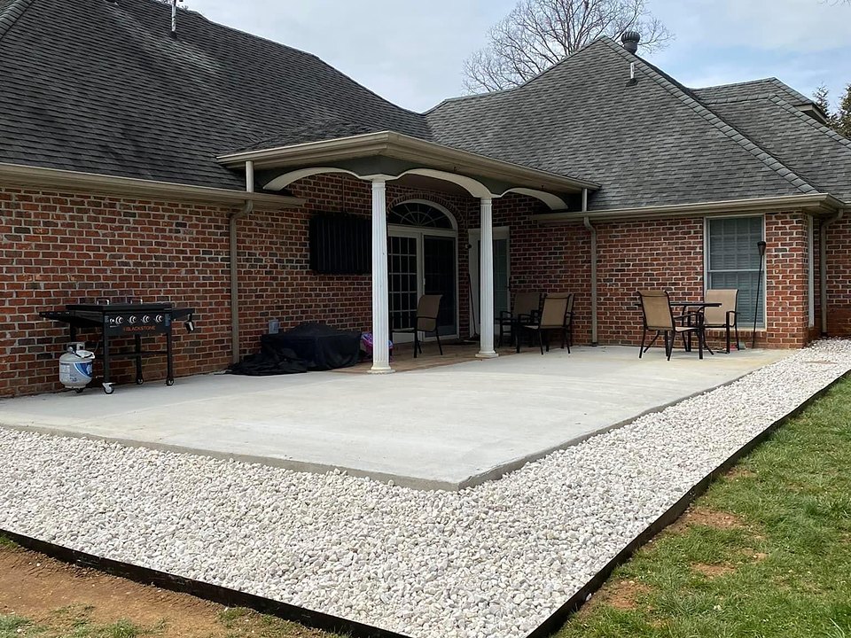 A newly poured concrete patio with a clean white-stone border behind a brick home, built by Cavalier Cleanup